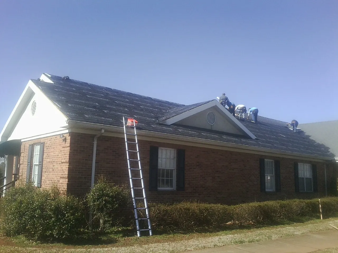 Crew tearing shingles off a brick ranch roof with a ladder set — Metal Roof Repair work by our crew in Newburg