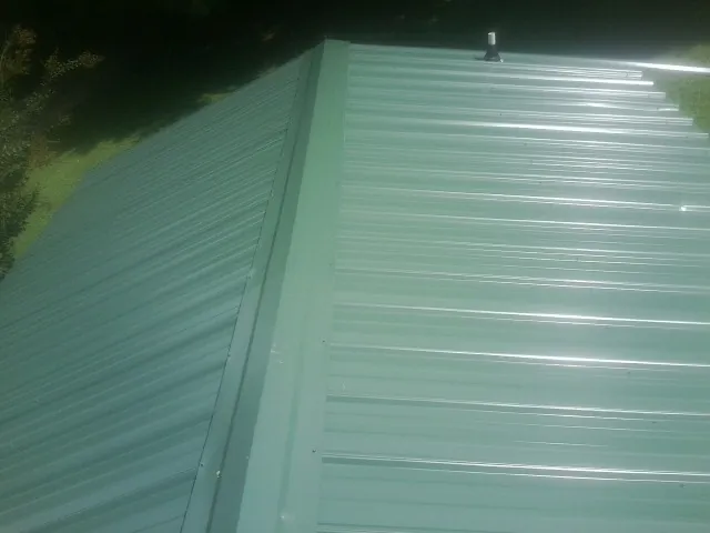 New green metal panels meeting at the ridge of a roof — Flat Roof Repair work by our crew in Newburg
