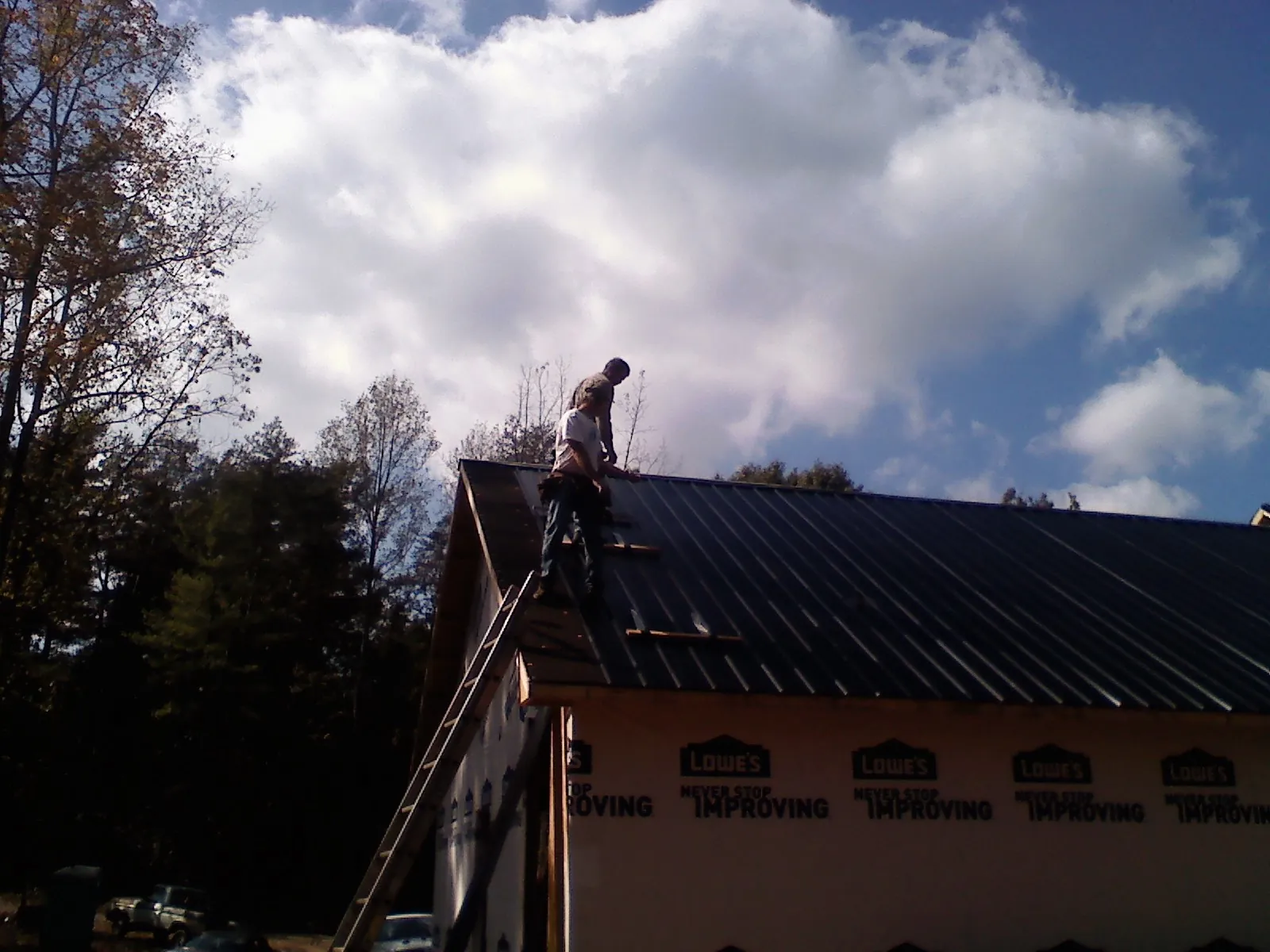Roofer fastening dark metal panels high against a cloudy sky, from a Roof Inspection job in Newburg