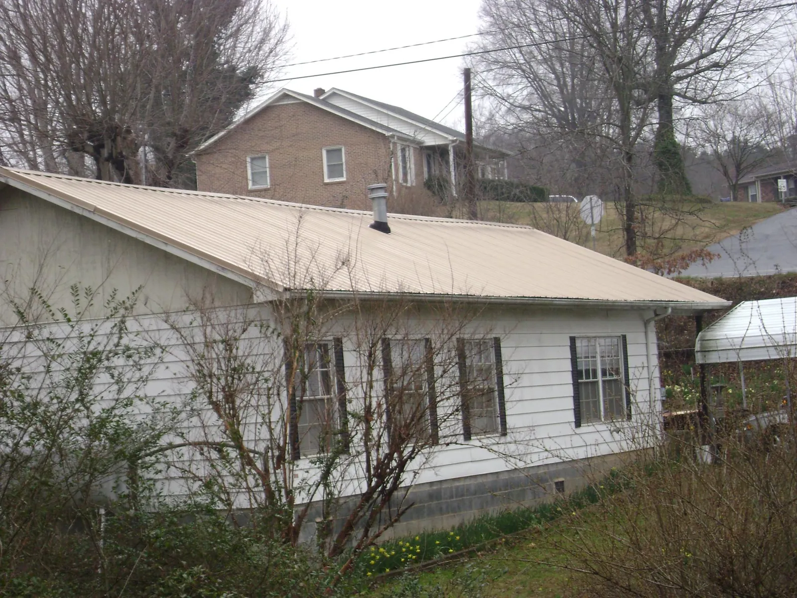 Tan metal roof on a white sided house set into a hillside — Commercial Roofing by Roofing Brothers in Newburg